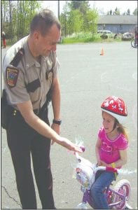 Right: State Patrol Trooper Aaron Schmidt gives Bridget Cooley a high five after she demonstrates that she knows bicycle hand signals. Far Right: Jack Corwin listens carefully to some bicycling advice from Burt Carlsted-Gillis. Staff photos/Brian Larsen